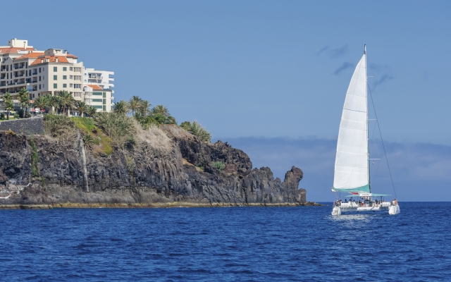 Pleasure catamaran sail close to the rocky shore.